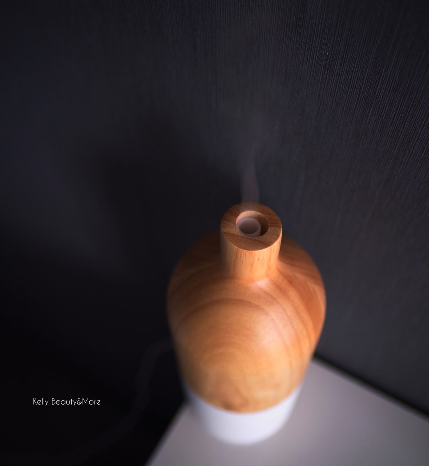 Houten aromaverstuiver met een wolkje damp tegen een donkere wand